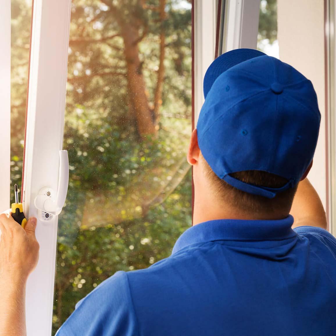 Person in a blue shirt and blue baseball hat installing a new window on a sunny day